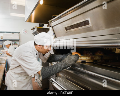 Lo Chef mettendo il pane nel forno Foto Stock