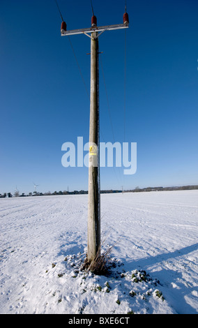 Singolo palo del telegrafo con un pericolo di morte segno su di esso. Da soli in una coperta di neve campo con un profondo blu cielo d'inverno. Foto Stock