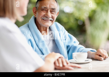 Senior uomo seduto a tavola con un infermiere Foto Stock