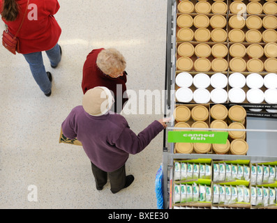 Due Signore anziane visto dall'alto shopping in un supermercato del Regno Unito, avendo una chiacchierata durante la scelta dei prodotti. Foto Stock