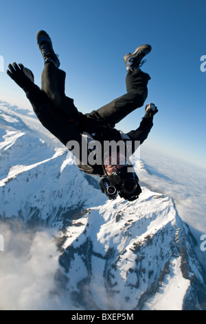 L'uomo con la fotocamera sul suo casco è filmare paracadutista in caduta libera su neve montagne. Foto Stock