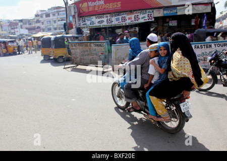 Musulmani indiani una famiglia di cinque persone sulla velocità di moto lungo una strada trafficata, ragazza indossare copricapo musulmano si guarda indietro in telecamera India Foto Stock