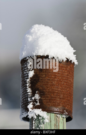 Coperta di neve arrugginito barattolo di latta sulla parte superiore del dipinto di verde recinto in legno pole Foto Stock