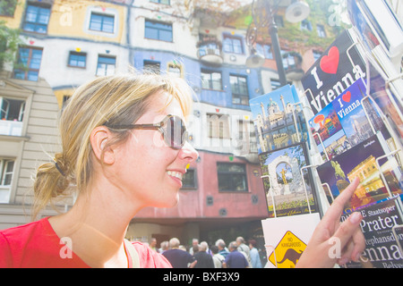 Donna che guarda le cartoline postali a Vienna con il famoso Hundertwasserhaus in background Foto Stock