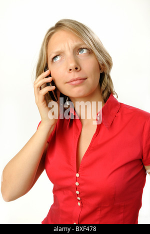 Giovane donna in una camicetta rossa di effettuare una chiamata su un telefono mobile e scettico espressione. Foto Stock