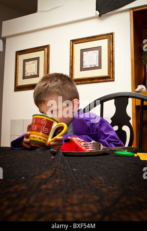 Un giovane ragazzo dolce mangiare e bere latte nel suo costume di Halloween Foto Stock