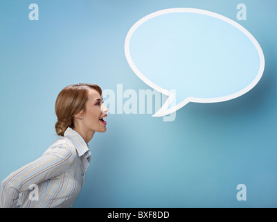 Adulto medio business donna urlando nel vuoto discorso bolla su sfondo blu. Sagoma orizzontale, vista laterale, vita, spazio di copia Foto Stock