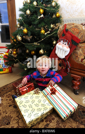 Baby boy apertura regali di Natale nella parte anteriore dell albero di Natale Foto Stock