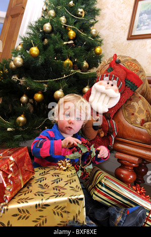 Baby boy apertura regali di Natale nella parte anteriore dell albero di Natale Foto Stock