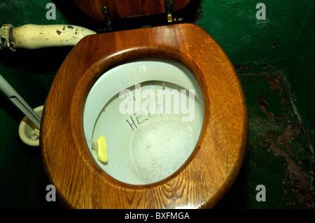 Vecchio wc con sedile in legno, con 'Help' scarabocchiati nel recipiente Foto Stock