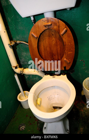 Vecchio wc con sedile in legno, con 'Help' scarabocchiati nel recipiente Foto Stock
