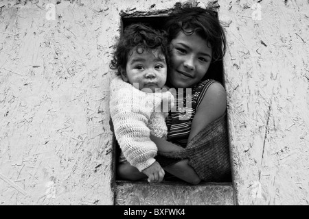 Spostato di una ragazza con la sorella del bambino guarda dalla finestra nella baraccopoli di Ciudad Bolívar, Bogotà, Colombia. Foto Stock