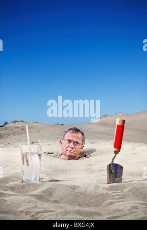 Uomo caucasico sepolto nella sabbia accanto al vetro di acqua e cazzuola Foto Stock