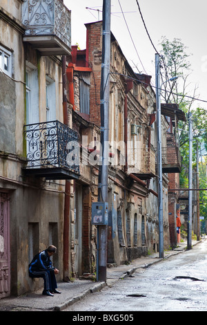 Uomo seduto sul davanzale in strada di tipiche case balconied a Tbilisi città vecchia, Kala, Georgia. JMH3981 Foto Stock