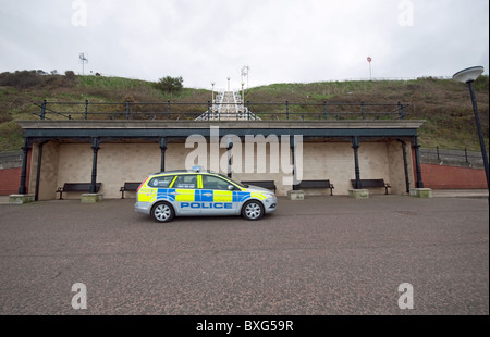 Rifugio in passeggiata sul lungomare con sedi in parcheggio auto con passaggio di auto della polizia. Foto Stock