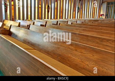 Questo stock immagine presenta righe di legno vuoti i banchi della chiesa con la luce del sole che filtra attraverso il verticale le finestre di vetro macchiate. Foto Stock