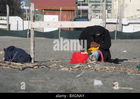 Mare di Ostia, nero senzatetto uomo dorme sotto il sole in un freddo pomeriggio invernale Foto Stock