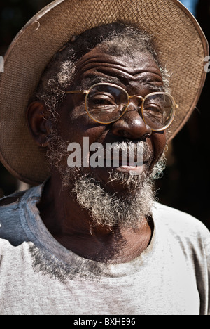 Il vecchio uomo con cappello di paglia e bicchieri guardando la telecamera, Chinotimba, Zimbabwe, Africa. Foto Stock