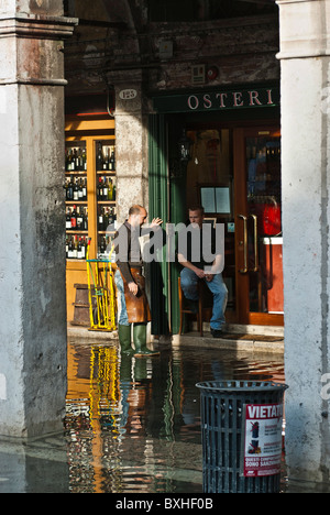 Le persone aventi una pausa in una strada allagata da "acqua alta", Venezia, Italia e Europa Foto Stock