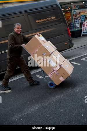 Un UPS uniti i pacchi servizio servizio di corriere uomo offrendo una pila di pacchi per un cliente, REGNO UNITO Foto Stock