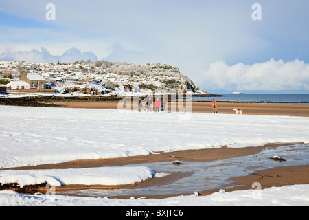 La gente camminare con i cani sulla spiaggia con la neve in inverno. Benllech, Isola di Anglesey, Galles del Nord, Regno Unito, Gran Bretagna Foto Stock