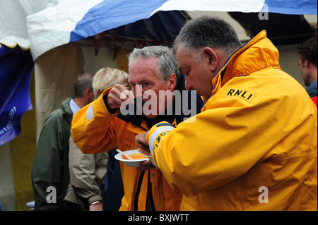 Due uomini dal RNLI godere un po' di zuppa di pesce durante il aberaeron festival di frutti di mare Foto Stock