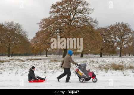Famiglia a piedi nella neve, mamma è di equitazione in slitta mentre papà lo tira lungo e spinge i due ragazzi nel loro buggy. Foto Stock