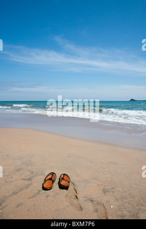 Paio di pantofole su una solitaria spiaggia di Nilaveli, Trincomalee, Sri Lanka East Coast, Pigeon Island in distanza. Foto Stock