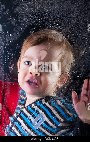 Little Boy gioca con la formazione di condensa sulla finestra Foto Stock