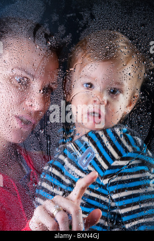 Little Boy gioca con la formazione di condensa sulla finestra Foto Stock