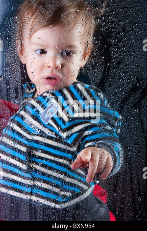 Little Boy gioca con la formazione di condensa sulla finestra Foto Stock