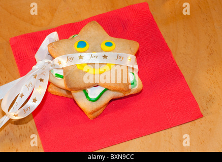 A forma di stella di Natale i biscotti con la glassa colorata legate con un nastro su un tovagliolo rosso Foto Stock