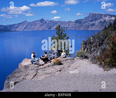 Vista lago con persone in alto sulla roccia a bordo del lago avente un picnic, Crater Lake - Cascades Mountain Range, Oregon, Stati Uniti d'America. Foto Stock