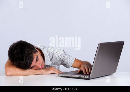 Giovane uomo dorme accanto al suo computer portatile (con sfondo grigio) Foto Stock