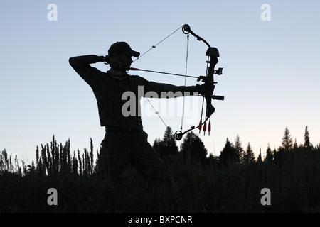 Silhouette di American Bow hunter disegno arco tornare nel bosco Foto Stock