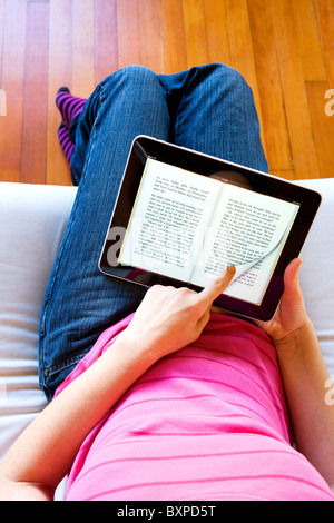 La donna in un momento di relax a casa utilizzando un Mac Apple iPad per leggere un libro da iBook sul suo grembo. Foto Stock