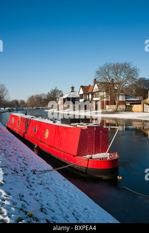 Uno rosso narrowboat lungo il fiume Cam con neve nelle banche contro un cielo blu Foto Stock