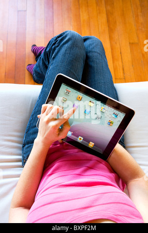 La donna in un momento di relax a casa utilizzando un Mac Apple iPad circa per utilizzare iTunes sul suo giro. Foto Stock