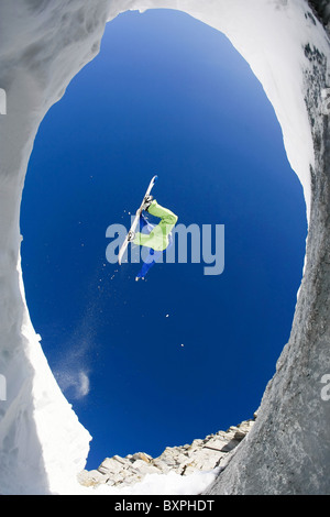Al di sotto di vista di intrepidi sportivo del salto in alto sulla montagne coperte di neve su snowboard Foto Stock