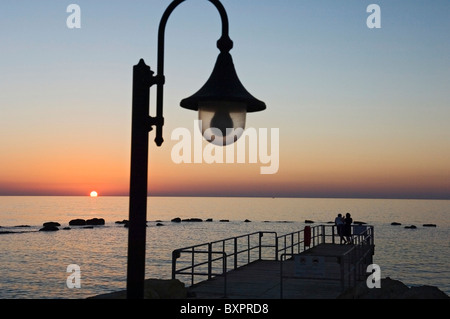 Un giovane su un piccolo molo di guardare il sole che tramonta in mare Foto Stock