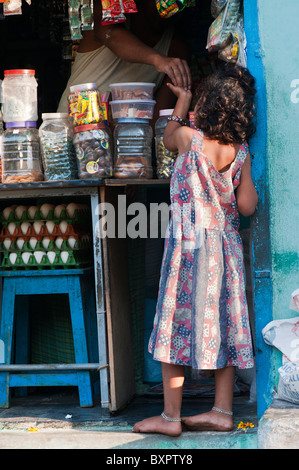 Piccola ragazza indiana la ricezione di cambiamento per le merci acquistate in un negozio del villaggio. Puttaparthi, Andhra Pradesh, India Foto Stock