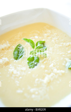 Zuppa cremosa di asparagi guarnita con parmigiano e basilico fresco in una ciotola bianca quadrata Foto Stock