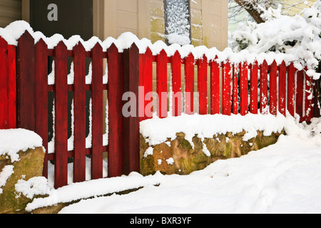 Recinto di picchetto di legno rosso e confine di cancello intorno ad una proprietà domestica del giardino nella neve. Regno Unito, Gran Bretagna. Foto Stock