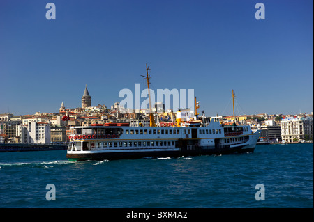 Una vista attraverso il Golden Horn verso la Torre di Galata a Istanbul con un traghetto in primo piano. Foto Stock