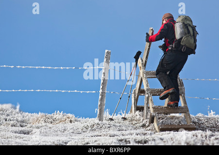 Nella valle di Chaudefour, un escursionista superando un cancello in inverno (Auvergne-France). Stile di legno. Foto Stock