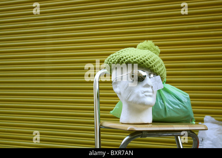 Manichino testa indossando occhiali da sole e un cappello verde contro un garage verde sullo sfondo della porta Foto Stock