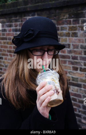 Un 15-anno vecchio ragazza adolescente sorseggia un Frapuccino Starbucks Coffee attraverso una paglia in una strada di Londra. Foto Stock