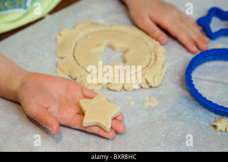 Bambino con le mani in mano il taglio di zucchero pasta biscotto al tavolo della cucina Foto Stock