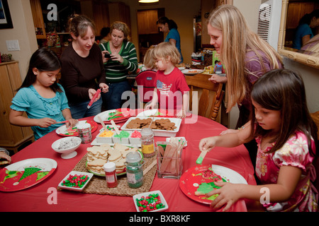 Le madri e i bambini si riuniscono intorno al tavolo della cucina per decorare biscotti di Natale a un partito dei cookie Foto Stock