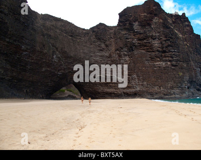 Due giovani donne in cammino verso l'arco, Honopu beach, costa di Na Pali, Kauai Foto Stock